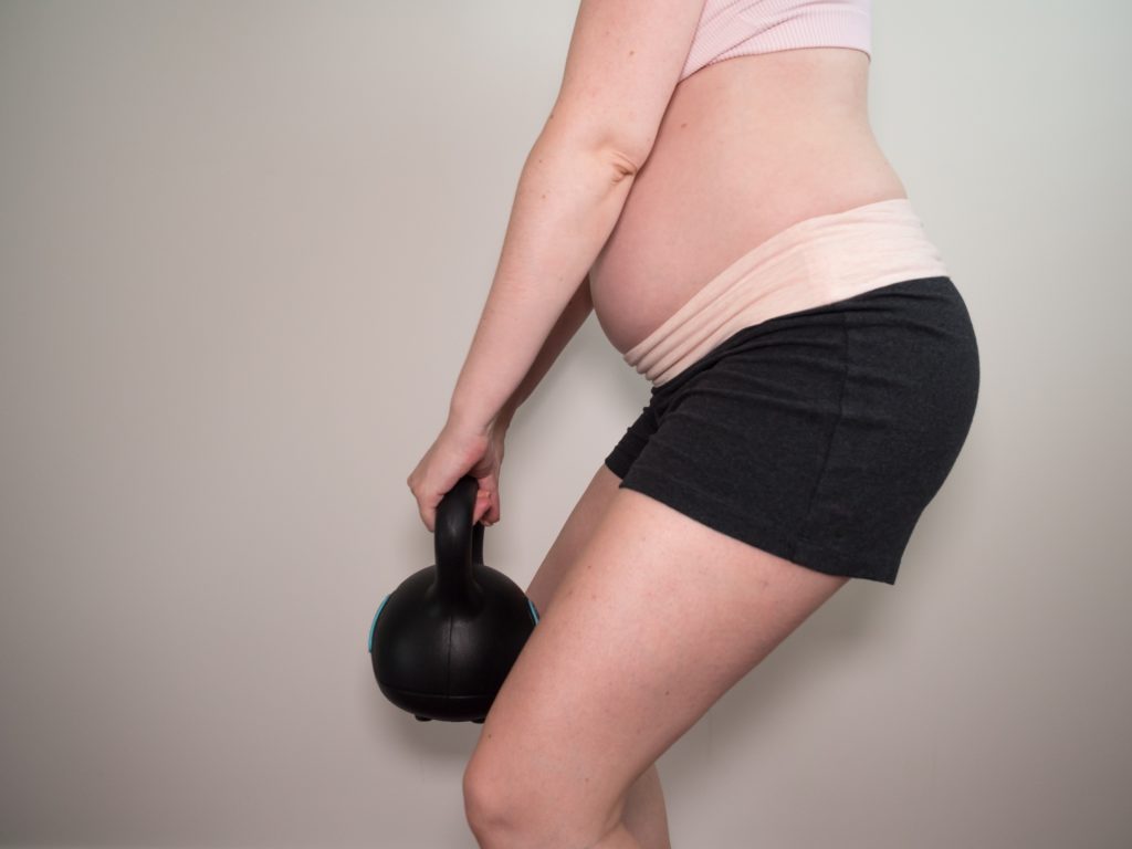 une femme enceinte fait de la musculation avec un kettelbell